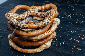 Fresh prepared homemade soft pretzels. Different types of baked bagels with seeds on a black background.