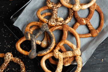 Fresh prepared homemade soft pretzels. Different types of baked bagels with seeds on a black background.