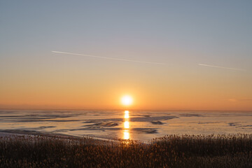 Scenic view of an orange sunset with sun reflecting in the ice of the lake. Motivational, inspirational view