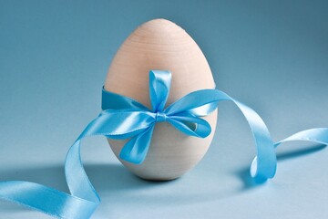 Wooden Easter Egg with Blue Bow and ribbon on light blue background with place for Your Text. Happy easter day. Close up. Banner