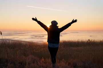 Woman silhouette with raised hand embracing the world on sunset. Freedom