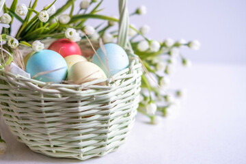 Baskets with Easter colored eggs on a white wooden table surrounded by delicate spring flowers