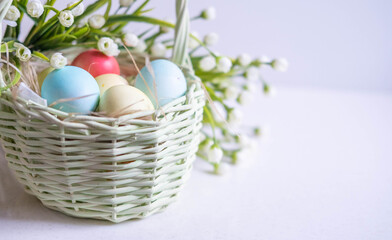 Fototapeta na wymiar Baskets with Easter colored eggs on a white wooden table surrounded by delicate spring flowers