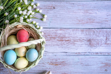 Baskets with Easter colored eggs on a white wooden table surrounded by delicate spring flowers