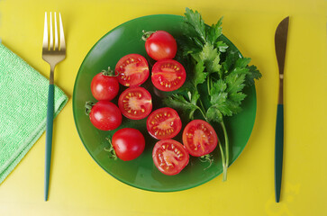 Sliced and whole cherry tomatoes with parsley in a green plate on a table with a yellow tablecloth. 