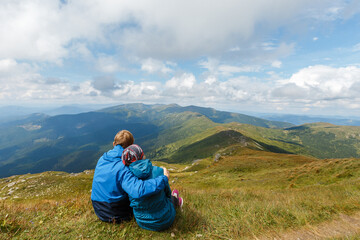 Couple sitting on mountain hill, hugging each other and looking on landscape. Man and woman romantic travel. Concept of hiking, active lifestyle and leisure at nature.
