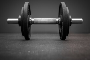 Fototapeta na wymiar Black and white photo of dumbbell bar loaded with weight plates on the floor at the gym. Bodybuilding equipment on a clean background with copy space. Fitness, weight training or health concept