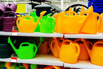 Plastic watering cans for watering flowers and plants are located in the shop window of the retail chain. Trade in accessories for gardeners. Мany objects. Selective focus © Dmitry
