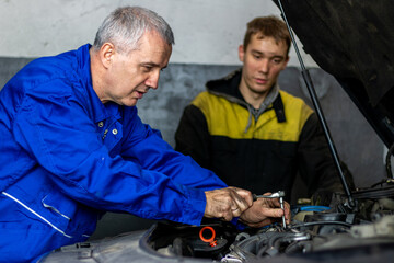 Fototapeta na wymiar Senior experienced mechanic teaches his colleague how to repair a car