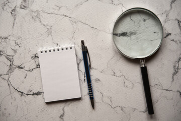 notes, lupa i długopis na marmurowym stole