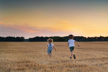 Fototapeta na wymiar Happy and free people, children run through the beveled field of wheat, people from behind