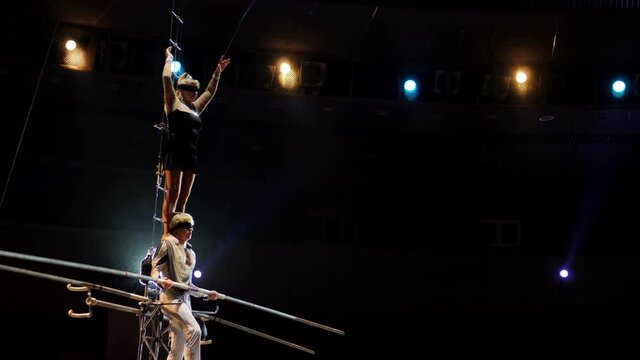 Performance of three aerial tightrope walkers gymnasts in white suits in the circus. Aerialists arrange a show for the audience under the dome of the circus, a tightrope walker walks on a rope.