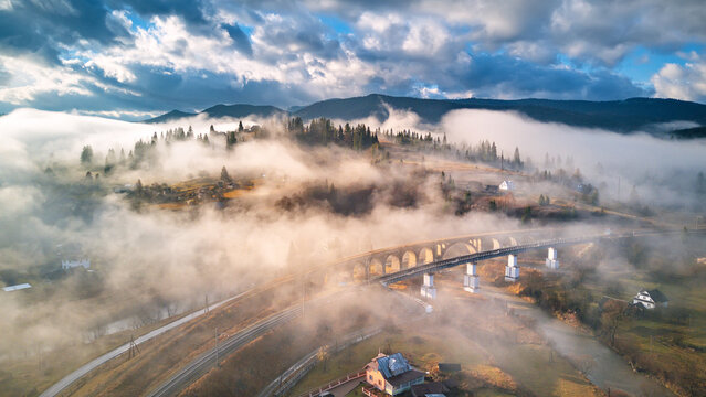 Autumn morning, foggy mountain valley. Railroad bridge, old viaduct in Vorohta. Village on hills covered by clouds.