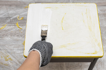 a hand holds a brush and paints the seat of a stool with it