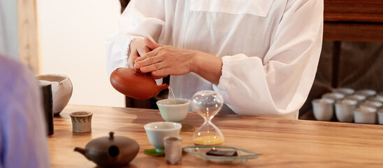 急須で湯呑み茶碗に緑茶を注ぐ割烹着姿の女性