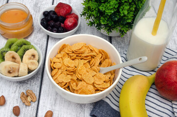 Corn flakes with milk and fresh banana, kiwi and apple, as well as fresh strawberries, blueberries and nuts. Healthy breakfast for the whole family.