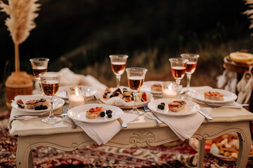 Food and Champaign Drink on Festival Vintage Table. Sliced Fruits and Berries on Bread Pieces Snacks, Alcoholic Beverage in Wineglass, Burning Candles and Utensil on Desk. Night Party with Friends