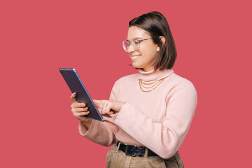 Profile view photo of happy young woman student using tablet over pink backdrop.