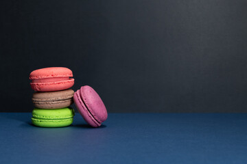 Close-up view of group of colourful french macarons lying on black and blue background. Pastry-shop. Copy space for your text. Confectionery theme.