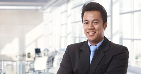 Confident young asian businessman smiling in modern business office. Portrait of adult man in 30s, happy confident smile. Copy space.