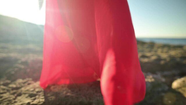 Close-up of red dress fabric on Caucasian attractive woman ripples in the wind. Walk on the sea in windy weather