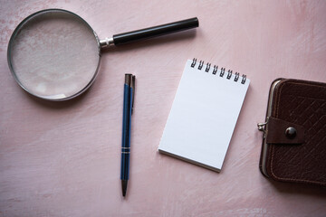 notes ,lupa długopis i brązowy portfel na różowym tle  - obrazy, fototapety, plakaty