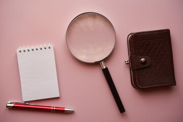 notes ,lupa długopis i brązowy portfel na różowym tle  - obrazy, fototapety, plakaty