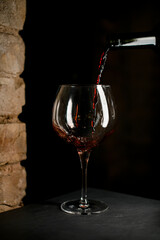Close-up of stemware for burgundy wine into which red wine is poured from a bottle.