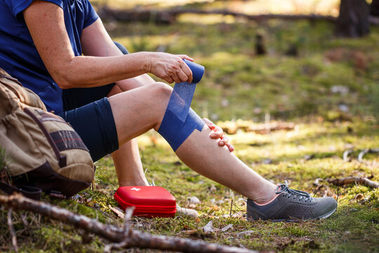 Injured hiker putting elastic bandage to her knee. Injury during hiking. First aid kit. Knee joint pain and tendon problems during adventure in nature
