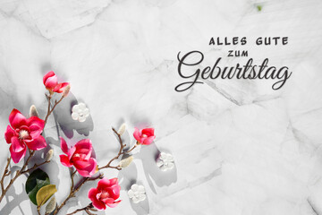 Springtime greeting card with pink magnolia twigs and white ceramic flowers on mint green stone. Text alles gute zum geburtstag means happy birthday in German language.