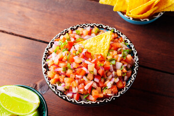 Bowl of Pico de Gallo and tortilla chips on brown boards. Pico de Gallo salsa and nacho chips. Mexican food. Top view