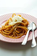 Un plato rosado de espaguetis frescos con salsa de tomate y queso parmesano