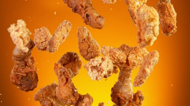 Super slow motion of flying fried chicken pieces hitting in the air, isolated on golden background. Filmed on high speed cinema camera, 1000fps. Speed ramp effect.