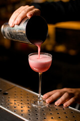 Fototapeta na wymiar hand of the bartender holds shaker and pours pink cocktail into glass