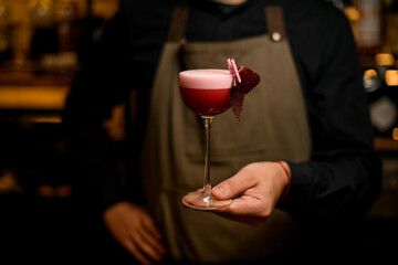 hand of bartender holds cocktail glass with foamy pink drink and decoration