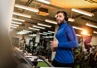 Fototapeta na wymiar Young man in sportswear running on treadmill at gym
