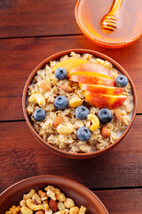 Tasty oatmeal with berries, nuts and apples on wooden table. Bowl of oatmeal porridge with blueberries and honey. Healthy breakfast. Top view