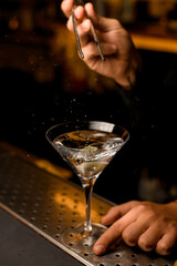 glass with a splashing martini cocktail and green olive is on the bar counter.