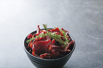 Bowl with spicy beef jerky on dark background