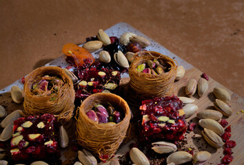 sweets with pistachios and dried fruits in baskets laid out on a wooden board on a brown background