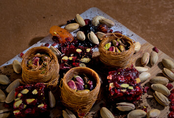 sweets with pistachios and dried fruits in baskets laid out on a wooden board on a brown background