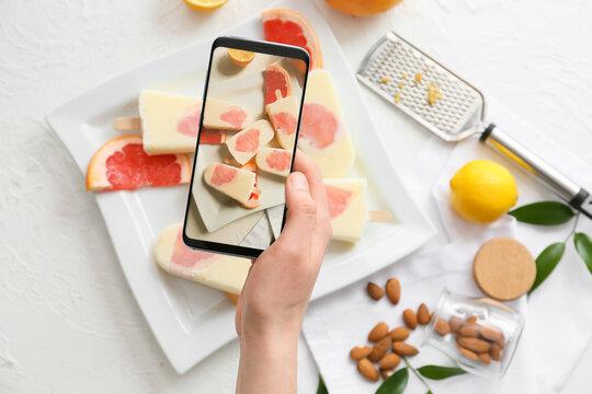 Woman with mobile phone taking photo of tasty citrus ice cream on table