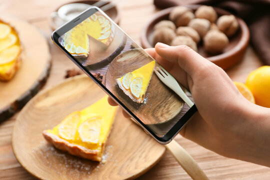 Woman with mobile phone taking photo of tasty lemon tart on table