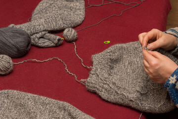 Fototapeta na wymiar Women's hands are knitting a sweater with knitting needles, next to it are balls of wool. The background is burgundy.