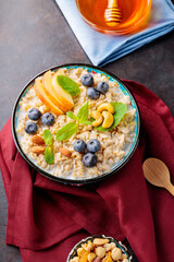 Oatmeal porridge with yogurt, berries and nuts on burgundy napkin. Bowl with oatmeal, blueberries, apples and honey on a dark background. Healthy breakfast. Top view