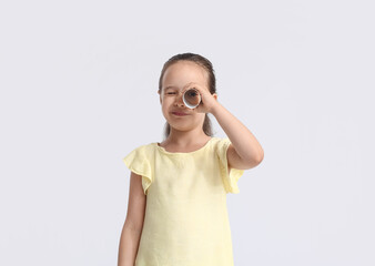 Cute little girl looking through tube of toilet paper on light background