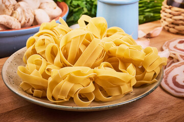 Traditional italian pasta - raw fettuccine nests in a plate on the kitchen table with ingredients for cooking pasta
