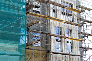 Fototapeta na wymiar Building under construction against blue sky. New high-rise building under construction with brick work and wooden scaffolding. Concrete building under construction. 
