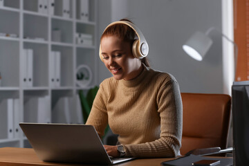Young woman with laptop listening to music at home in evening