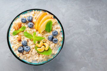 Oatmeal porridge with apple slices and fresh mint. Oatmeal bowl with blueberry and nuts on a gray background. Top view. Copy space